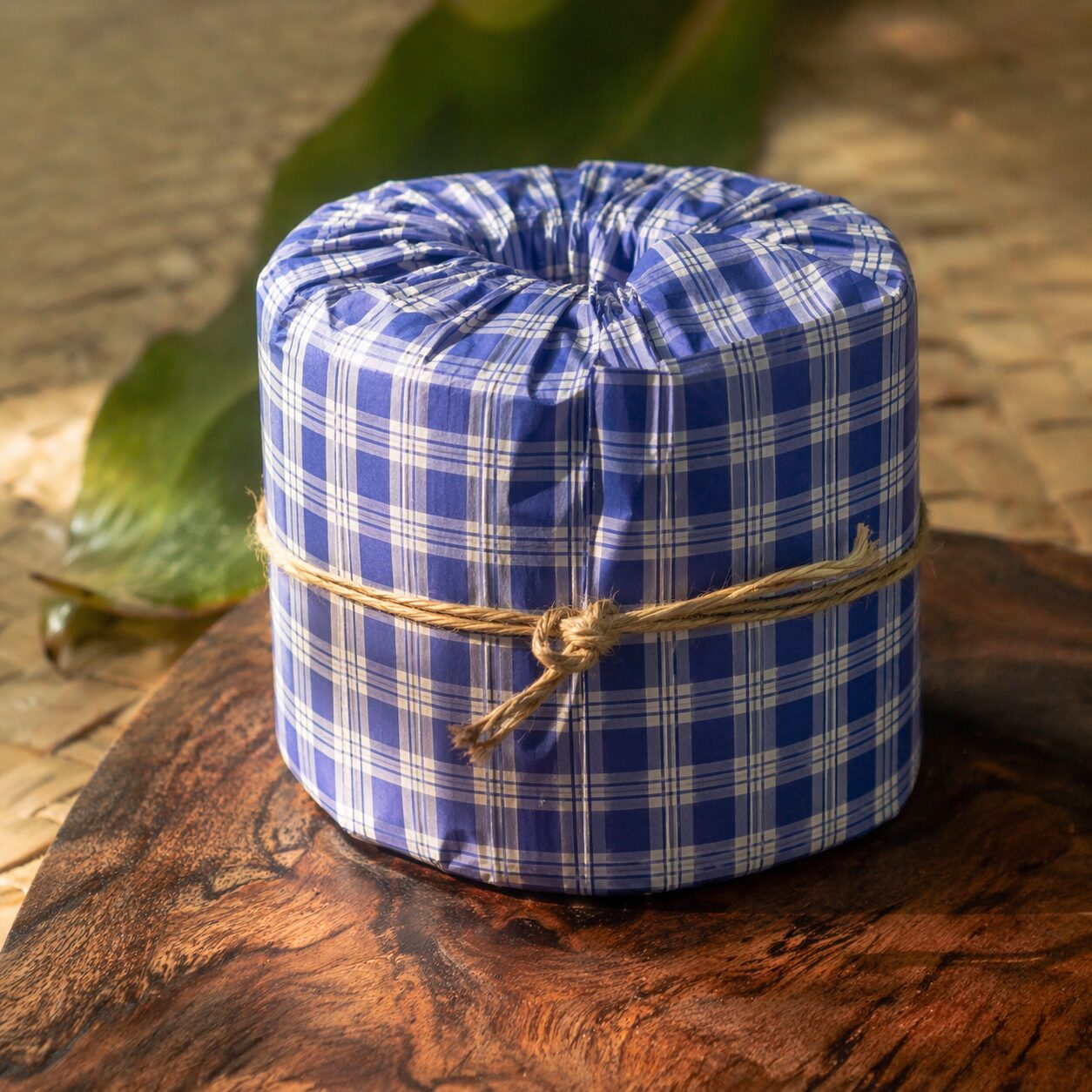 Close-up of a single palaka-wrapped bamboo toilet paper roll tied with natural cordage, resting on koa wood